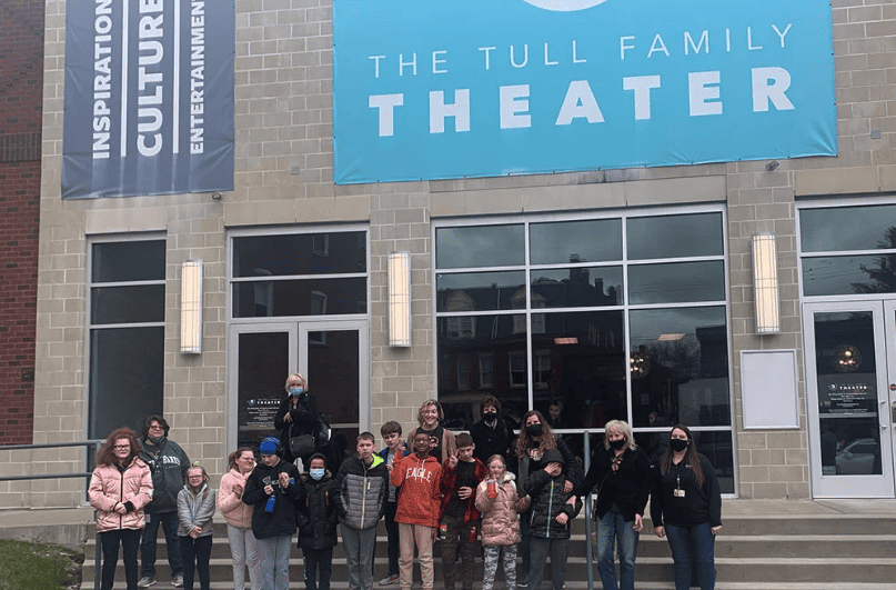 A group of school children gather in front of the Tull Family Theater doors and sign