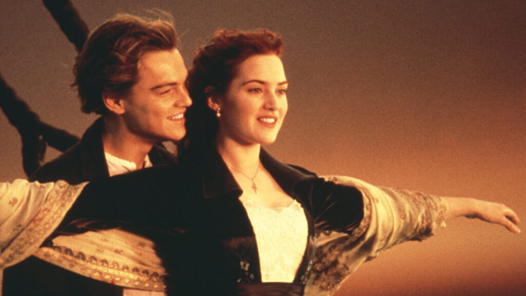 Two main characters of the movie titanic standing on the bow of the ship at sunrise.