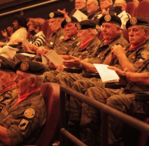 A group of Vietnam veterans, wearing their military uniform, sit applauding inside the theater