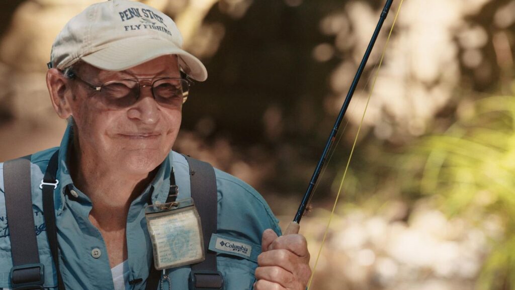 Man in his 80s holds a fishing rod and smiles